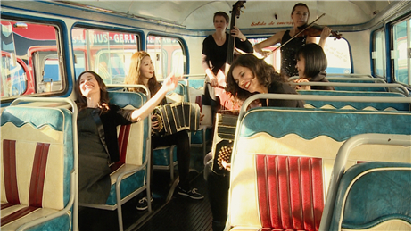 영화의 한 장면으로 보인다. 아주 오래된 외국의 버스 안에 여성 6명이 각자의 악기를 연주하고, 노래하고 있다.