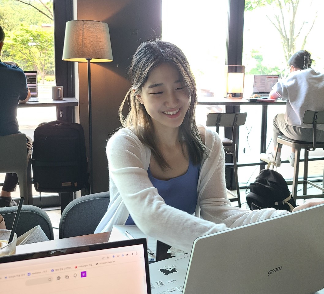 세련된 카페에서 찍은 사진. 그램 노트북 화면을 보며 미소짓는 여자가 있다.